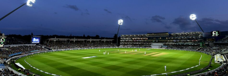 Floodlit cricket stadium with players on the field and spectators in the stands